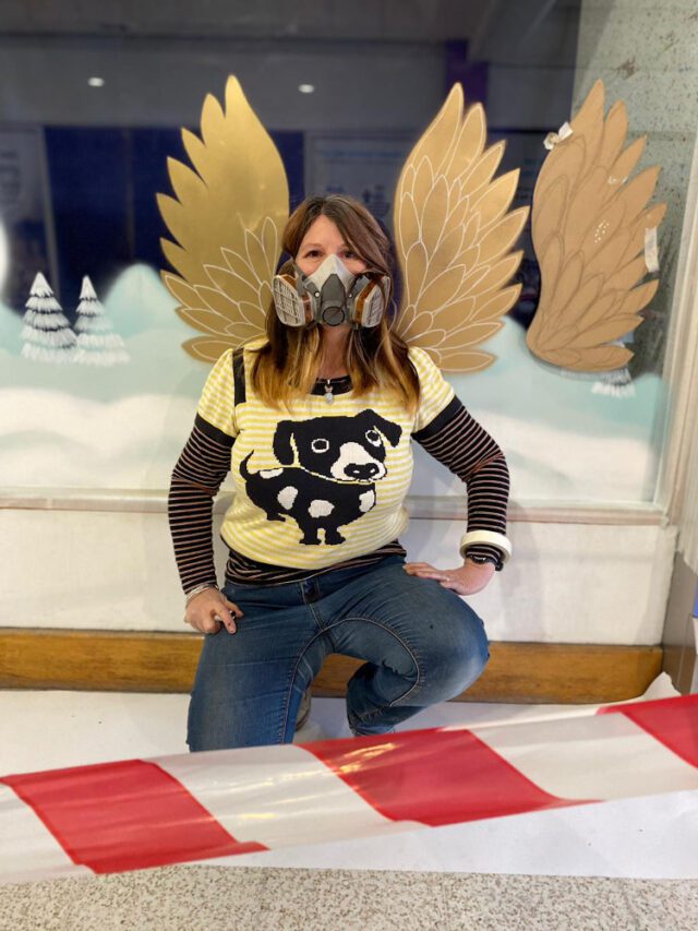 Wearing safety painting mask and sitting in front of gold colour angel wings spray painted onto a shop window