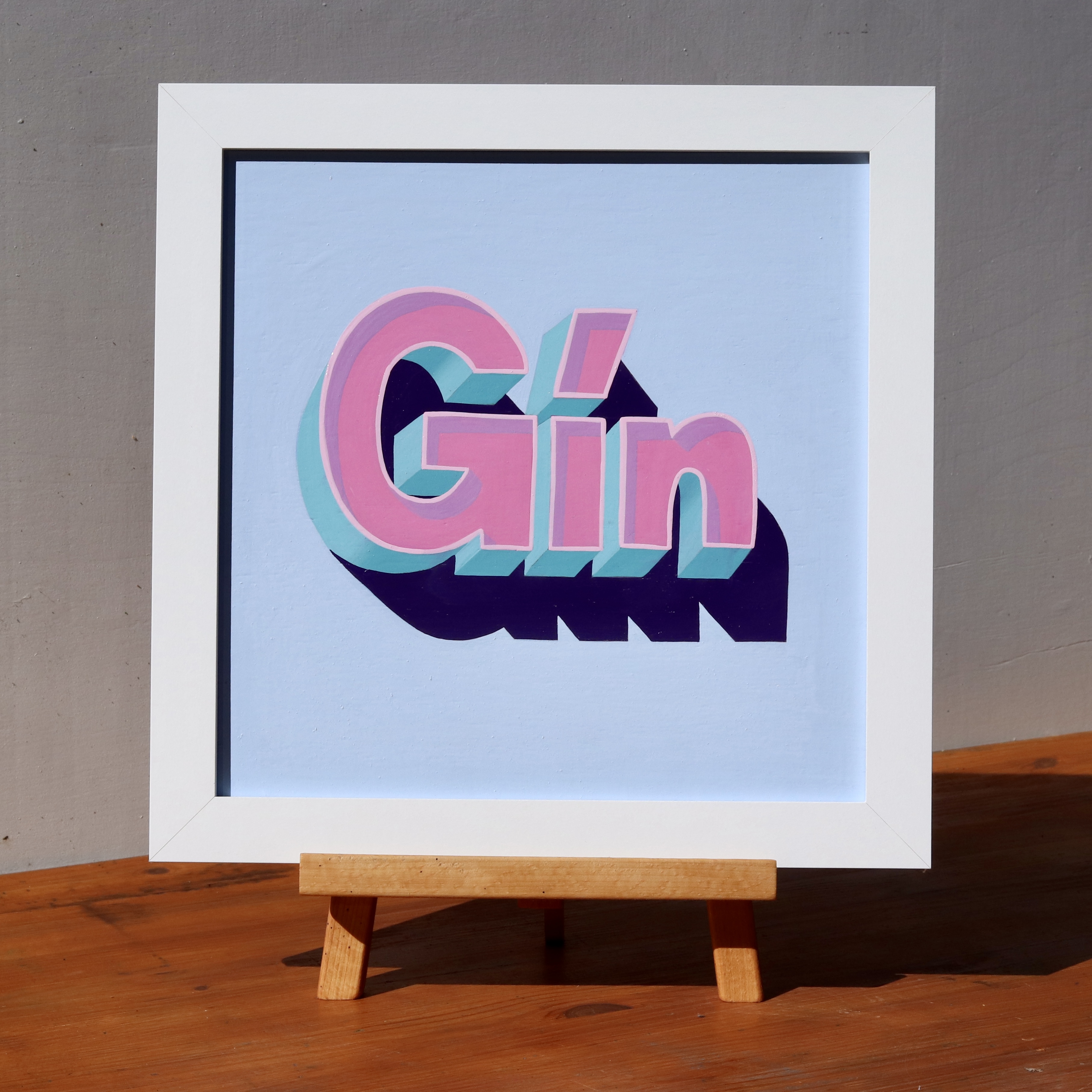 'GIN' hand lettered and painted wall art sign in 3D effect block lettering, magenta and turquoise on a baby blue background, in a white wooden frame