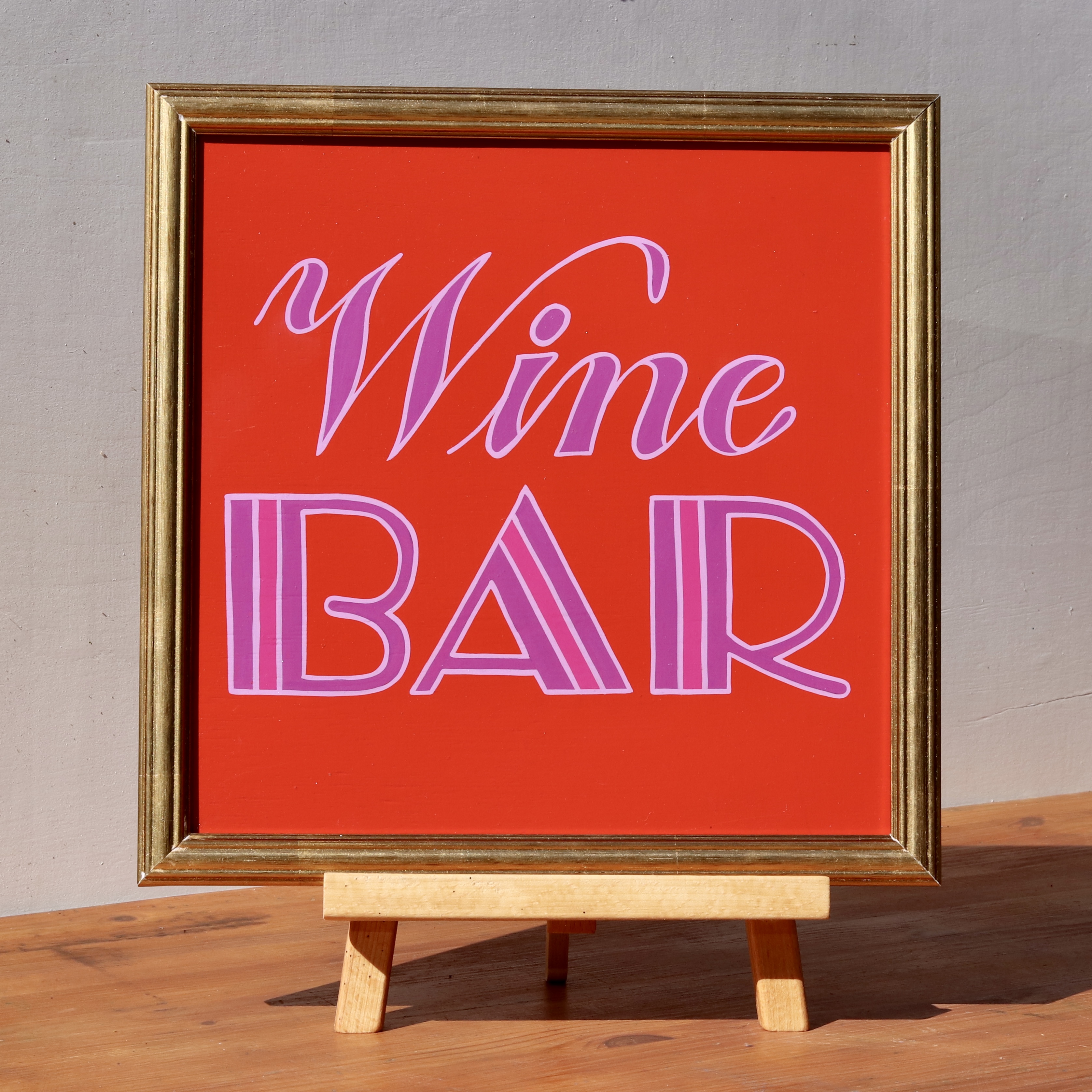 'Wine Bar' framed wooden hand-painted word art sign script and art deco style hand lettering in lilac and purple on a red background