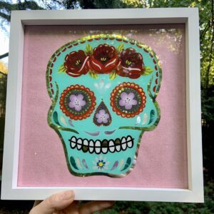 Sugar Skull artwork hand-painted in aqua blue enamel on the reverse of glass, featuring canal roses, white gold leaf, shell inlay and a pink glitter background and finished in a white wood frame