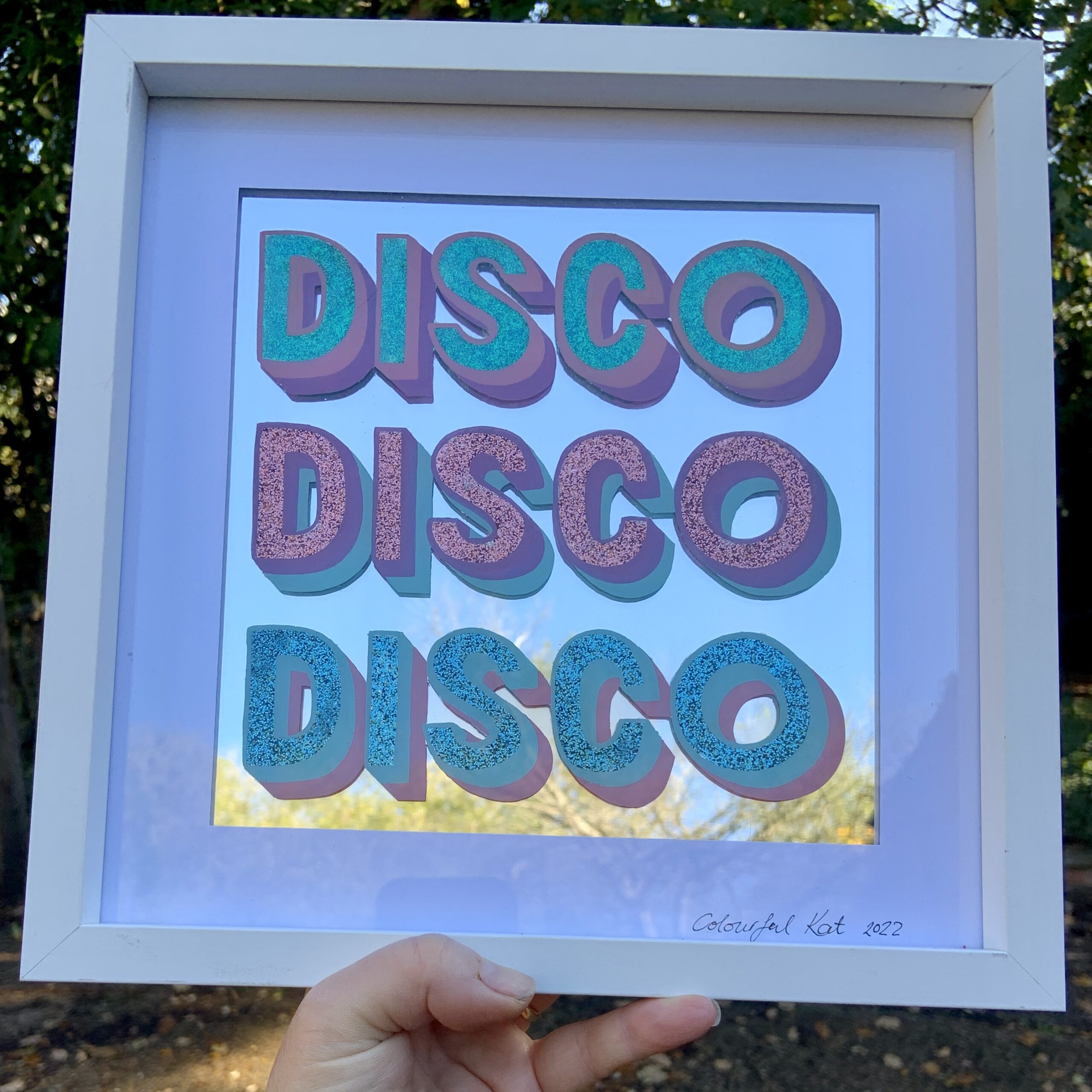 'Disco Disco Disco' handpainted lettering in pastel blue, pink, violet paint and glitter applied on the back of glass with a mirror background, framed in white wood with white card mount