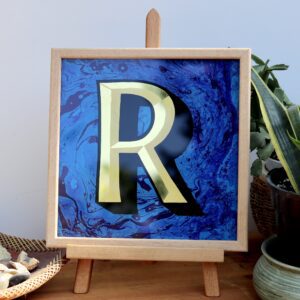 Reverse Glass gilded letter R in 23carat yellow gold and blue marbled backgrounddisplayed on a an easel