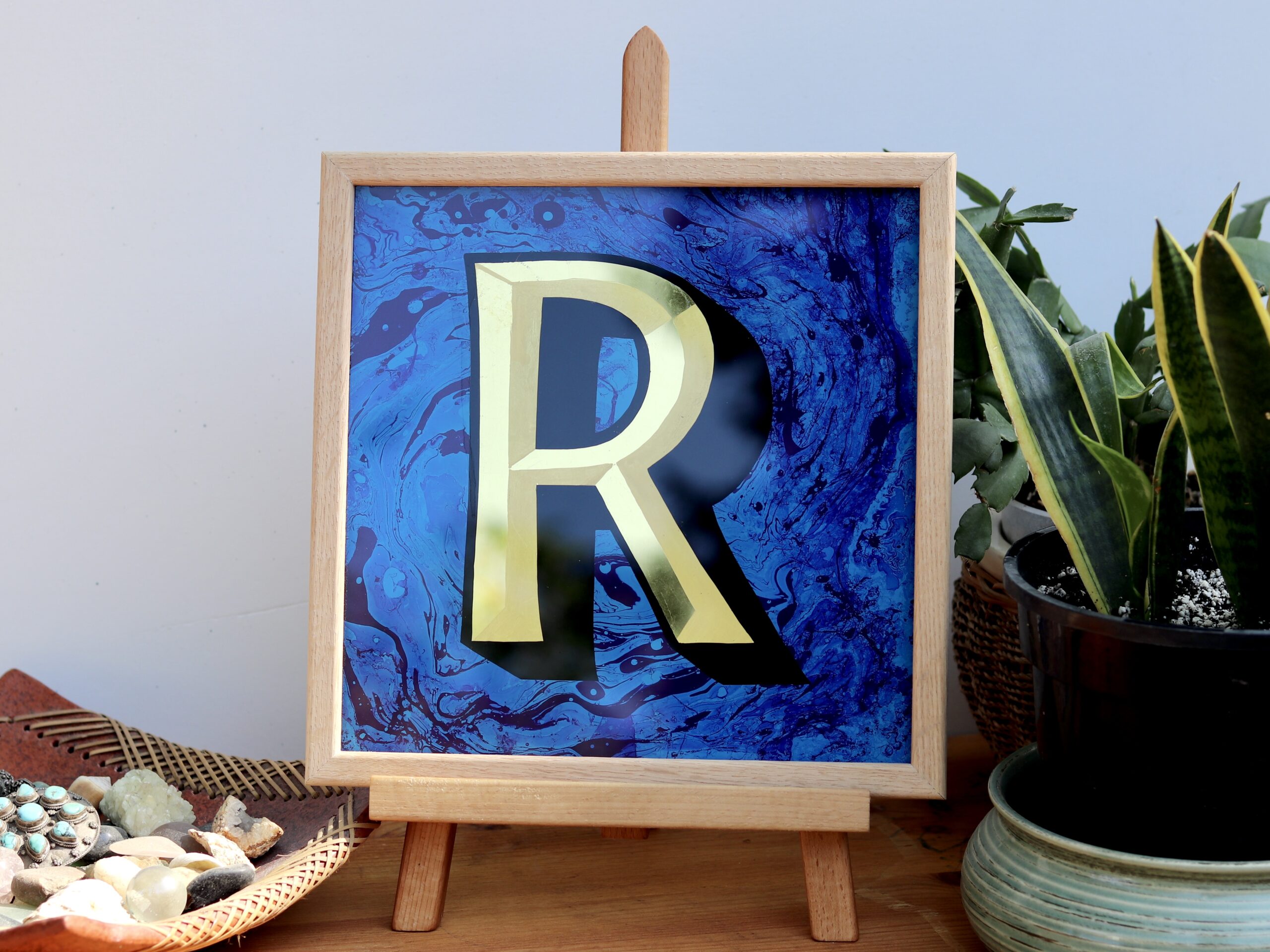 Reverse Glass gilded letter R in 23carat yellow gold and blue marbled backgrounddisplayed on a an easel