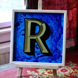 Reverse Glass gilded letter R in 23carat yellow gold and blue marbled background