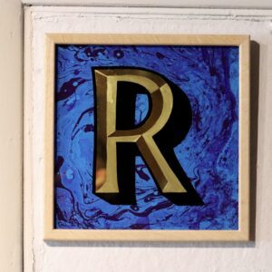 Reverse Glass gilded letter R in 23carat yellow gold and blue marbled backgrounddisplayed on a white wall