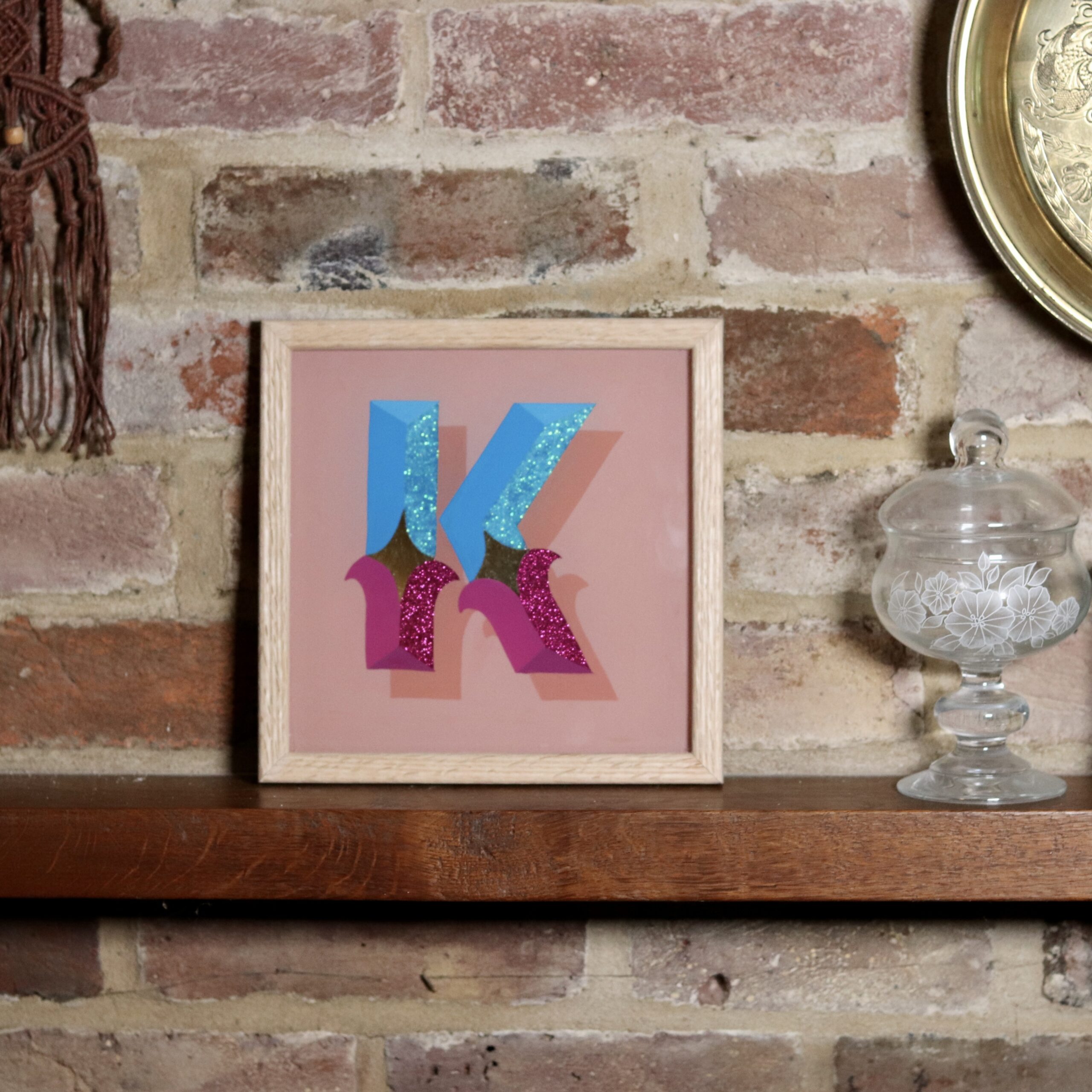 Framed reverse glass gilded circus style letter K in blues, violets, gold and glitter