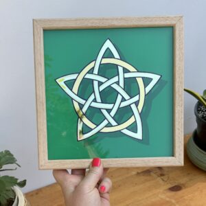 Hand holding a stunning gold leaf mirror effect 5 pointed celtic knot star in 2 colours of genuine gold leaf on a green background and framed in oak wood