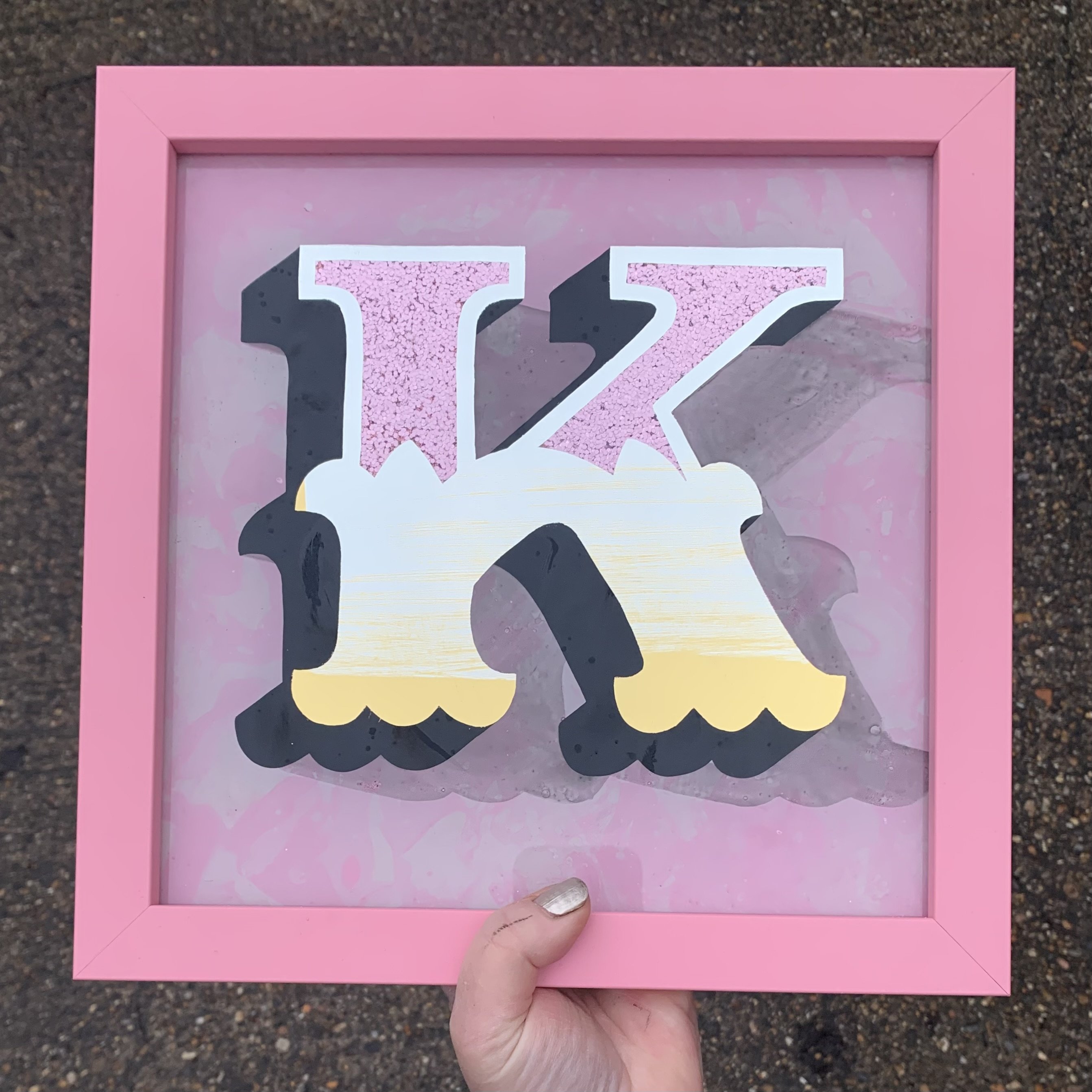 Stunning reverse glass gold leaf circus style letter K handcrafted in 18ct white gold leaf blended into 23ct yellow gold leaf, infilled with pink glitter, completed on a marbled paint background and finished with a pink wood frame