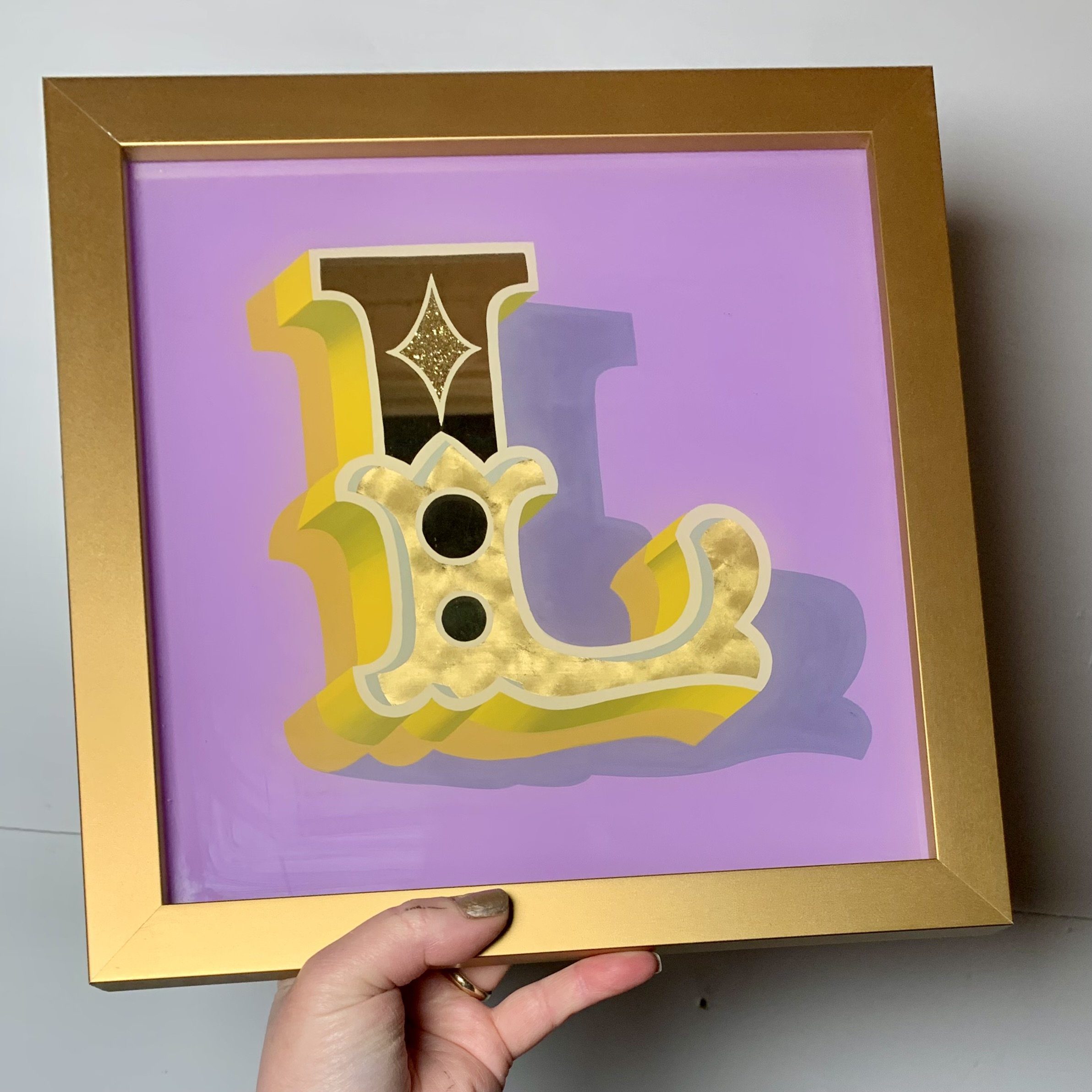 Stunning reverse glass gold leaf circus style letter L handcrafted in 18ct lemon gold leaf using oil & water gilding techniques, paint blending and finished in a gold coloured wood frame