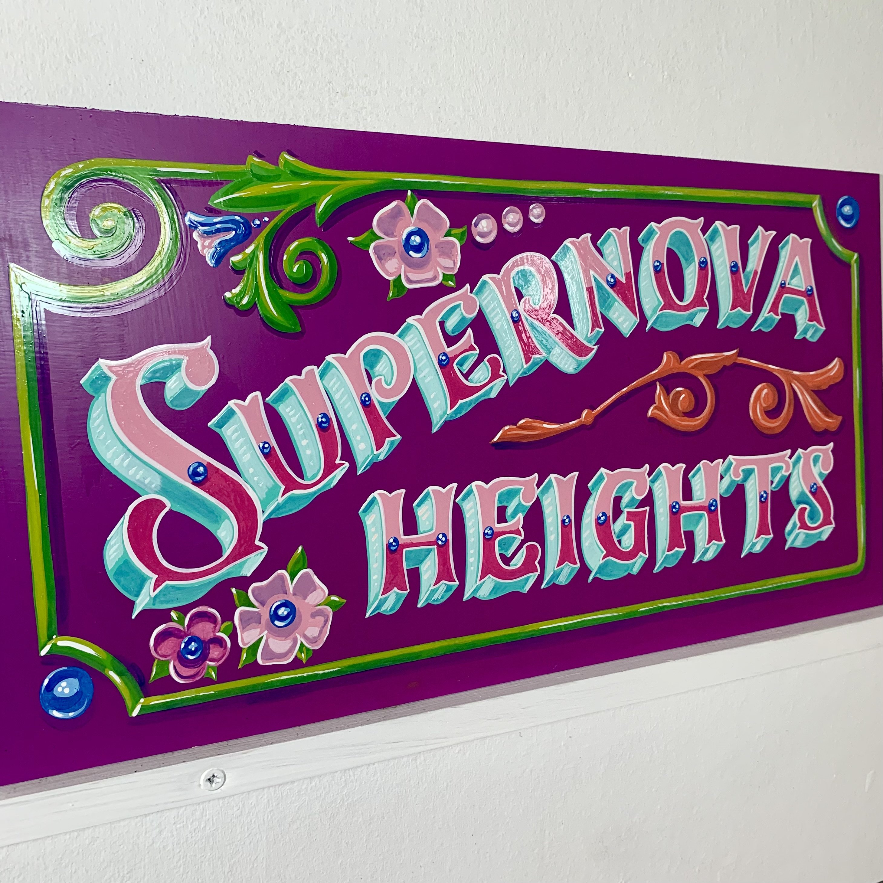 Supernova Heights hand lettered and painted in Argentinian fileteado style in purple, with blue, green and orange accents