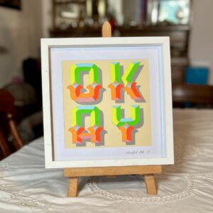 OKAY papercut letter art in neon green orange pinks and yellow in white frame