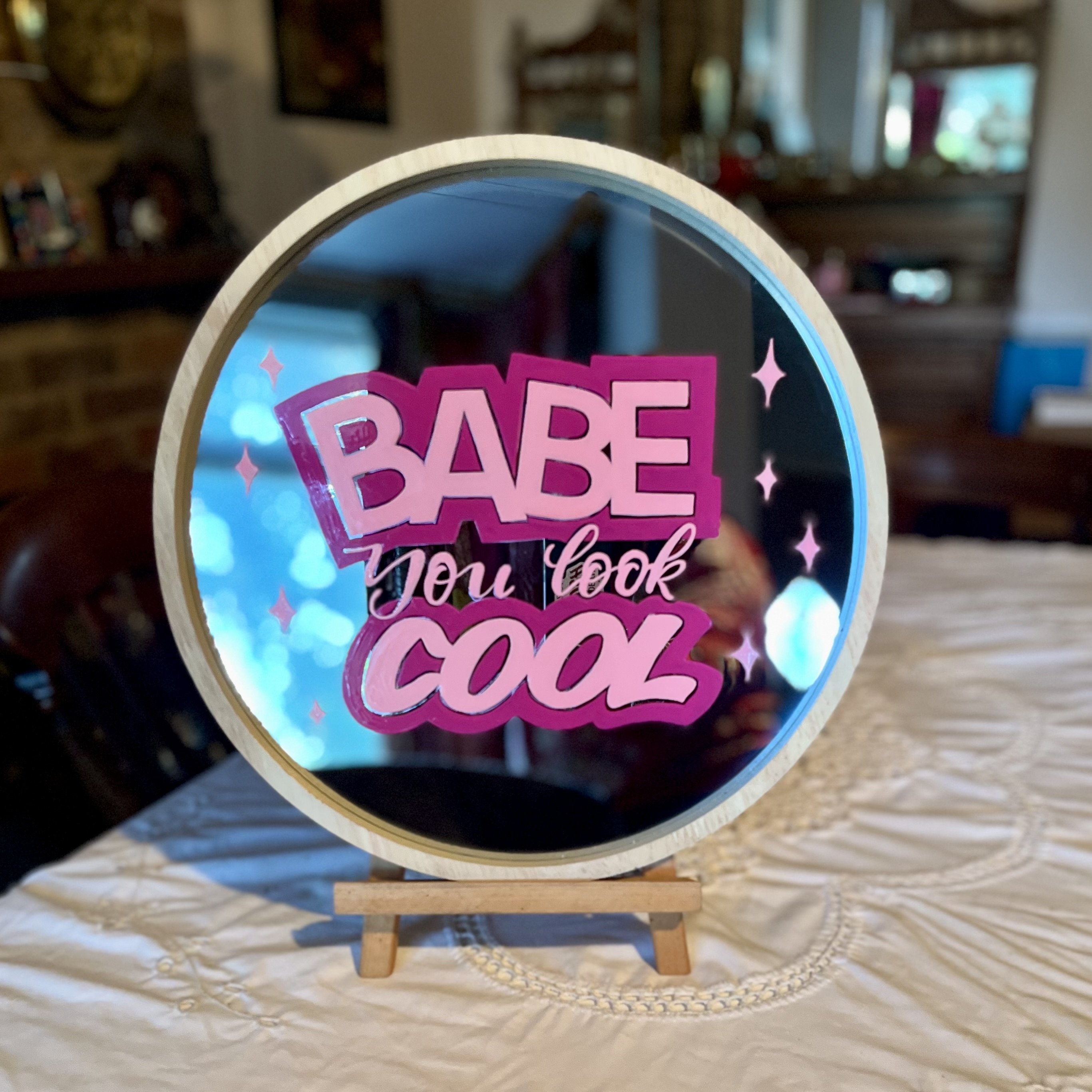 'Babe you look Cool' signwritten onto round mirror with a white frame in pink and magenta signwriting enamels