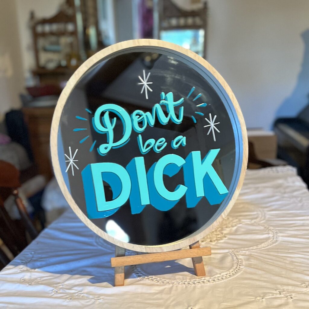 'Don't be a Dick' signwritten onto round mirror with a white frame in light teal and dark teal signwriting enamels