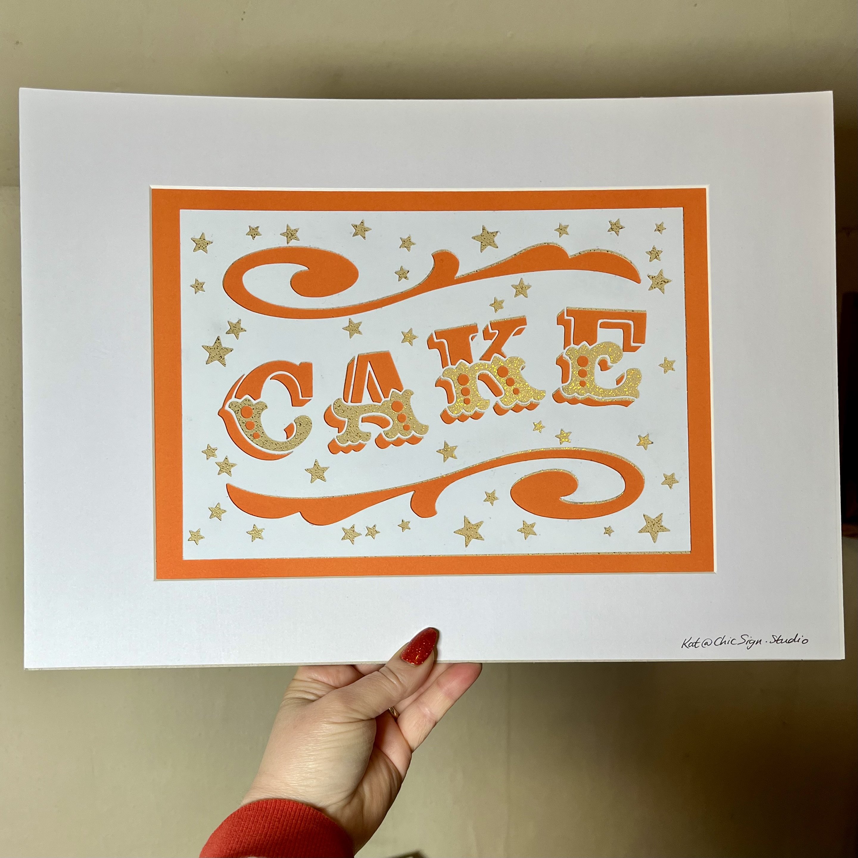 CAKE handfinished papercut lettering artwork with window mount and backing board in orange, white & gold card