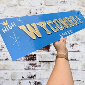 Handpainted sign WYCOMBE in Rizla paper style painted in metallic brass, white and black on a light blue background